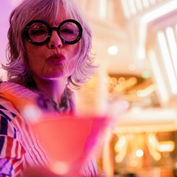 Kvinde med solbriller nyder drink i Celebrity Cruises martini bar med farvet stemningslys