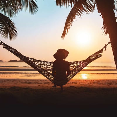 Kvinde sidder i hængekøje ved solnedgang og kigger på havet i Thailand