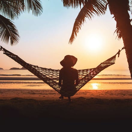 Kvinde sidder i h&aelig;ngek&oslash;je ved solnedgang og kigger p&aring; havet i Thailand