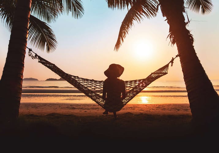 Kvinde sidder i h&aelig;ngek&oslash;je ved solnedgang og kigger p&aring; havet i Thailand
