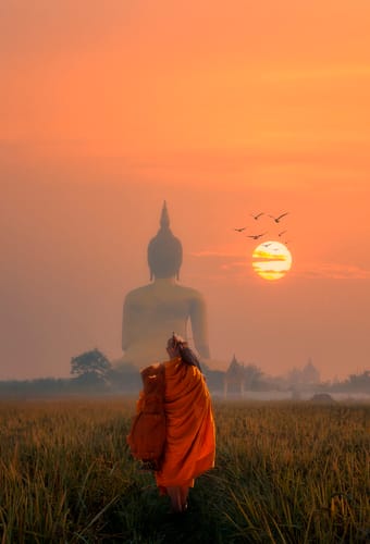 Munk g&aring;r mod stor buddha figur i solnedgang i thailand
