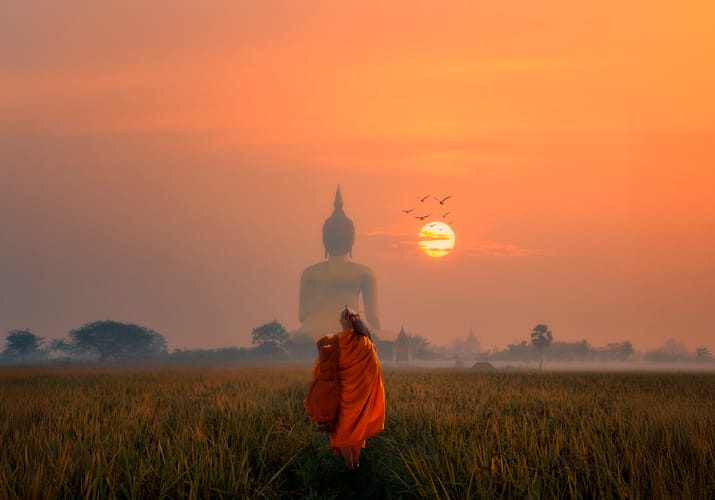 Munk går mod stor buddha figur i solnedgang i thailand