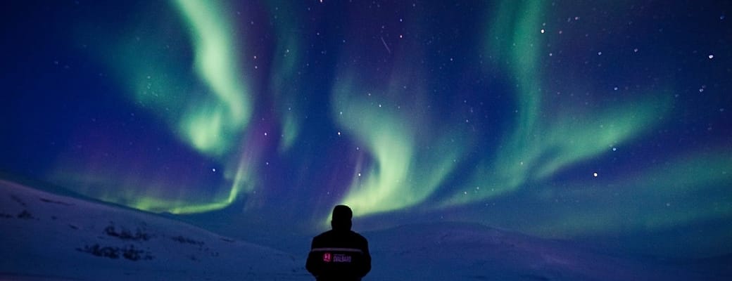 Mand i termotøj beundrer nattenhimlen med nordlys i grønt