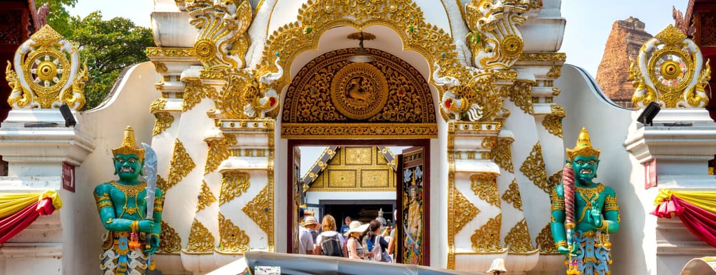Traditionel bl&aring; tuk-tuk parkeret foran farverigt thailandsk tempel med gulddetaljer og gr&oslash;nne tempelvogter-statuer