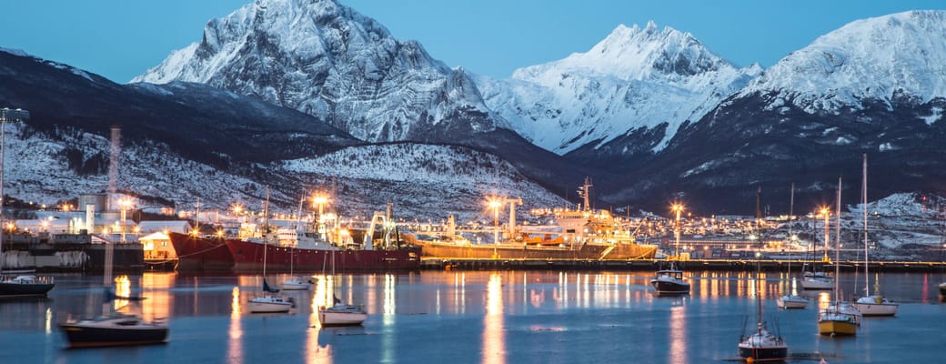 Aftenlys over Ushuaia med oplyst havn, både og snedækkede bjerge i Patagonien