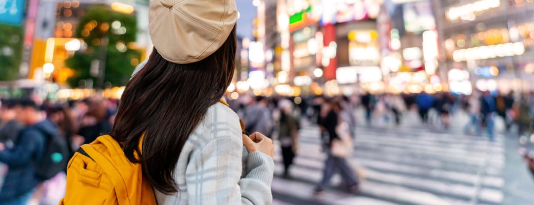 Kvinde fotograferer Shibuya Crossing i Tokyo om aftenen med neonlys og folkehavet