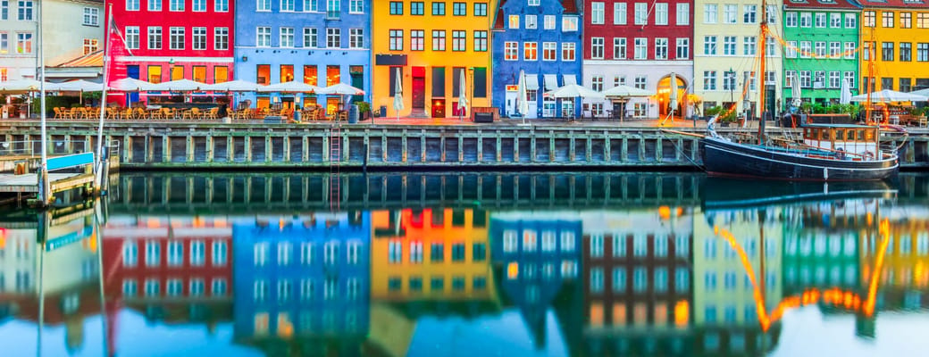 Farverige huse og restauranter langs Nyhavn i K&oslash;benhavn spejlet i kanalen