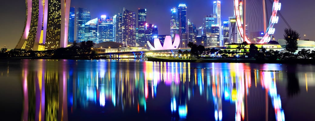 Malaysia Singapore skyline om aftenen med oplyst Marina Bay Sands og Singapore Flyer reflekteret i vandet
