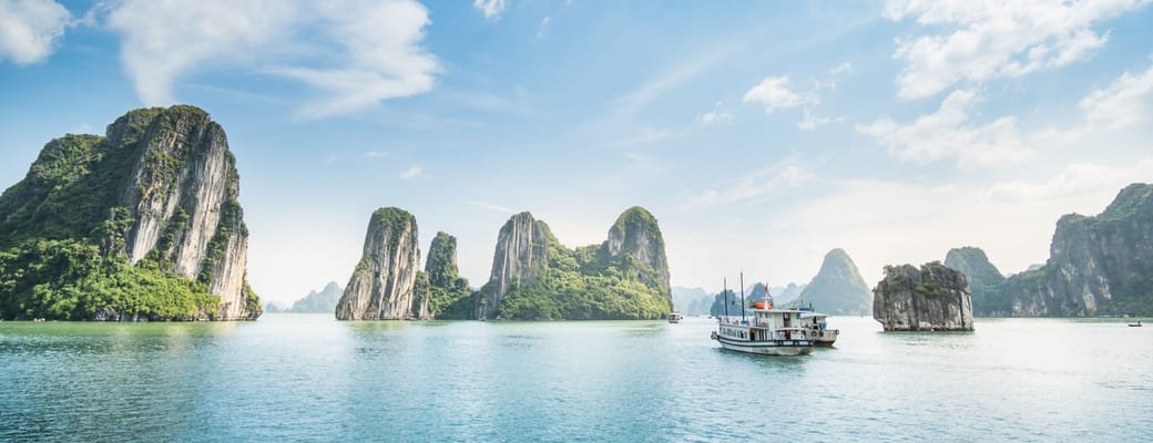 Dramatiske kalkstens&oslash;er i Halong Bay Vietnam med traditionel b&aring;d sejlende i smaragdgr&oslash;nt vand