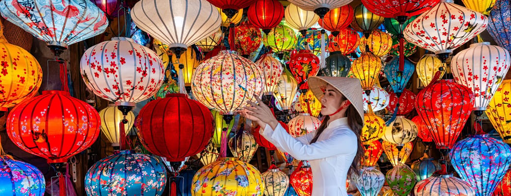 Kvinde i hvid &aacute;o d&agrave;i blandt hundredvis af farverige vietnamesiske lanterner i Hoi An, traditionelt marked med r&oslash;d, gul og bl&aring; lanterner