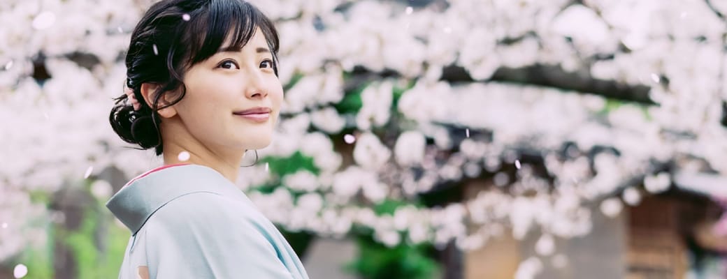 Kvinde i kimono st&aring;r blandt blomstrende kirseb&aelig;rtr&aelig;er i for&aring;ret i Japan
