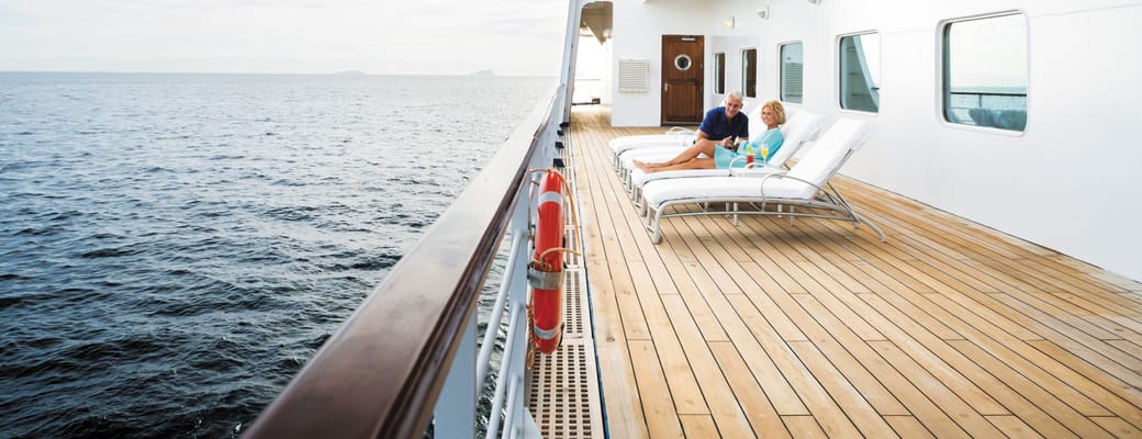Par slapper af på liggestole på krydstogtskibet Regent Seven Seas Voyager med udsigt til åbent hav