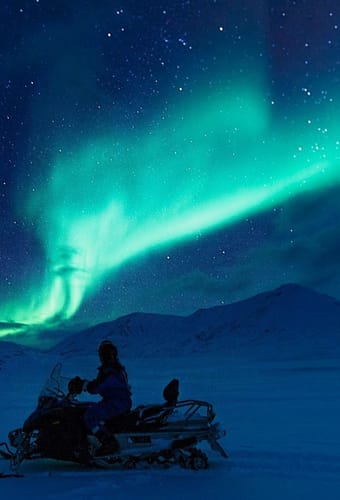 Snescooter på tur i den blå time med grønt norslys på himlen