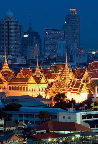 Grand palace lyser gyldent op foran skyskrabere i tusm&oslash;rke i Bangkok i Thailand