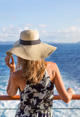 Kvinde med hat ved rælingen ombord på Norwegian Escape krydstogtskibet – dag på havet
