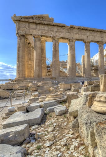 Parthenon på Akropolis i Athen, omgivet af antikke søjler og ruiner under blå himmel
