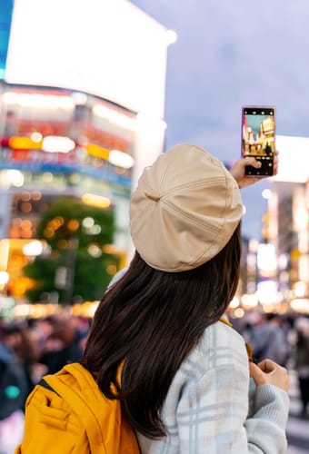 Kvinde fotograferer Shibuya Crossing i Tokyo om aftenen med neonlys og folkehavet