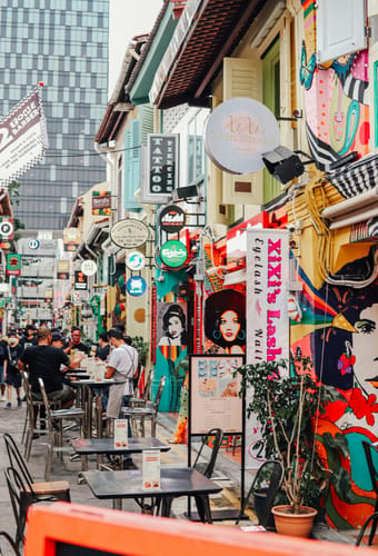 Livlig gade i Singapore med farverige caféer, skilte og gæster der spiser udendørs