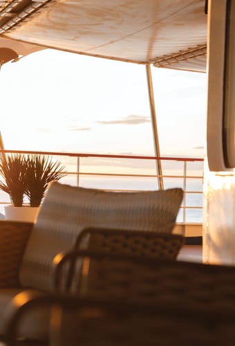 Hyggelig lounge på dækket i solnedgang med kurvestole, planter og udsigt til havet