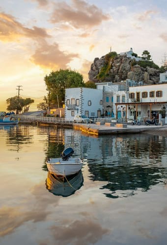 Hyggelig havnefront i Patmos by ved solnedgang med tavernaer, hvide huse og lille b&aring;d i vandet