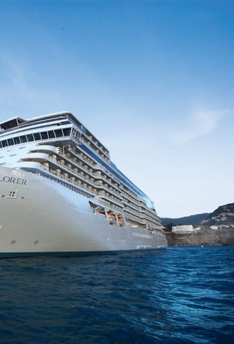 Krydstogtskibet Seven Seas Explorer set fra st&aelig;vnen med kyst og klipper i baggrunden
