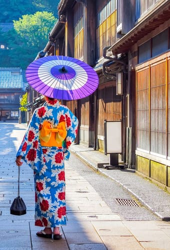 Person i farverig kimono med parasol går gennem traditionel gade i Kanazawa i Japan