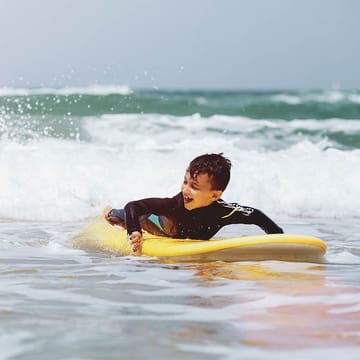 Dreng som surfer i vandet i Portugal