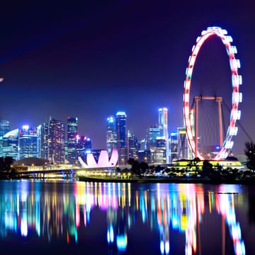 Malaysia Singapore skyline om aftenen med oplyst Marina Bay Sands og Singapore Flyer reflekteret i vandet