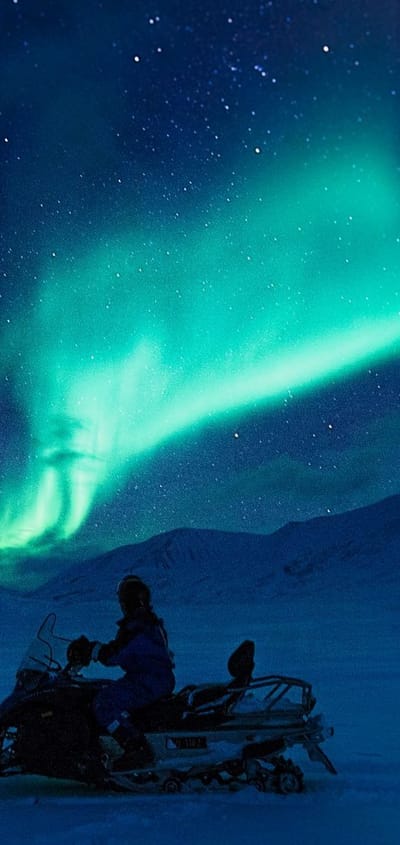 Snescooter på tur i den blå time med grønt norslys på himlen