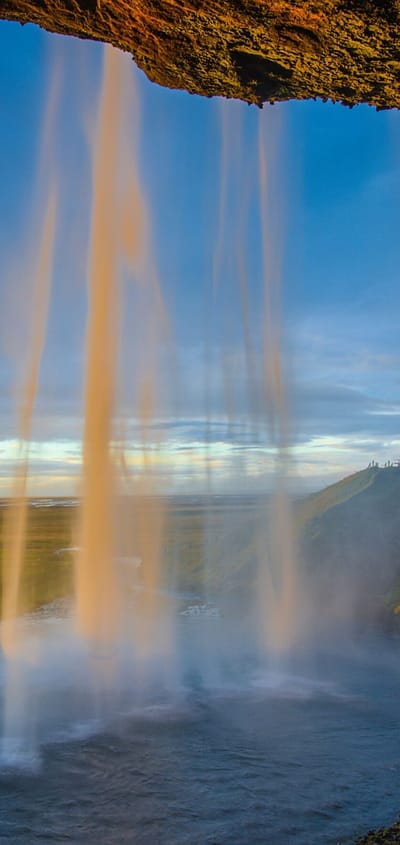 Seljalandsfoss vandfald på Island ved solnedgang med gyldent lys gennem vandfaldet og grønne marker i baggrunden