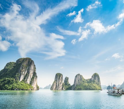 Dramatiske kalkstensøer i Halong Bay Vietnam med traditionel båd sejlende i smaragdgrønt vand