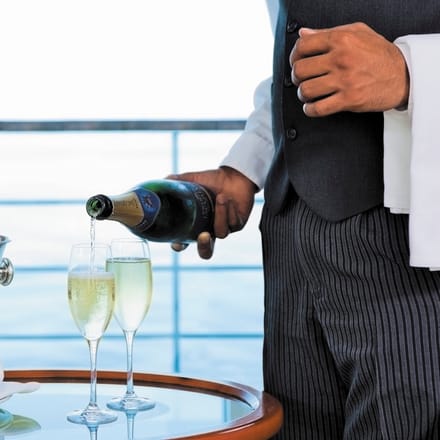 Butler serverer champagne i suite med havudsigt p&aring; Regent Seven Seas Cruises