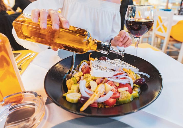 graekenland kvinde haelder olivenolie over salat