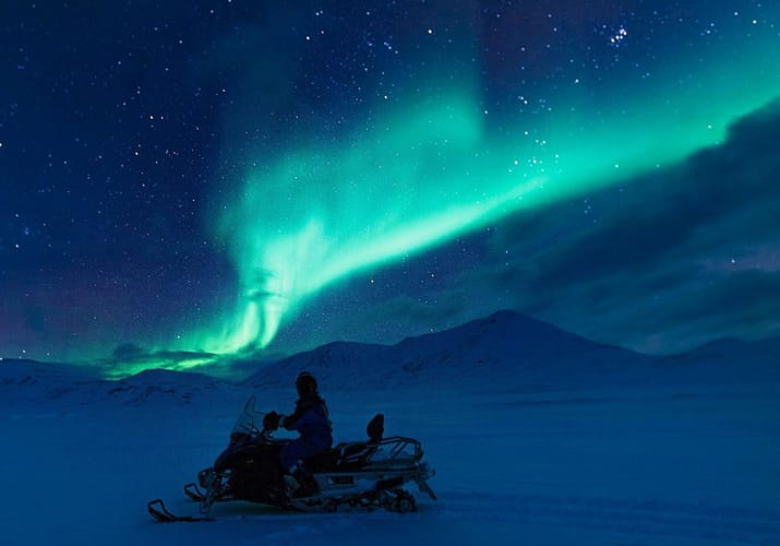Snescooter på tur i den blå time med grønt norslys på himlen