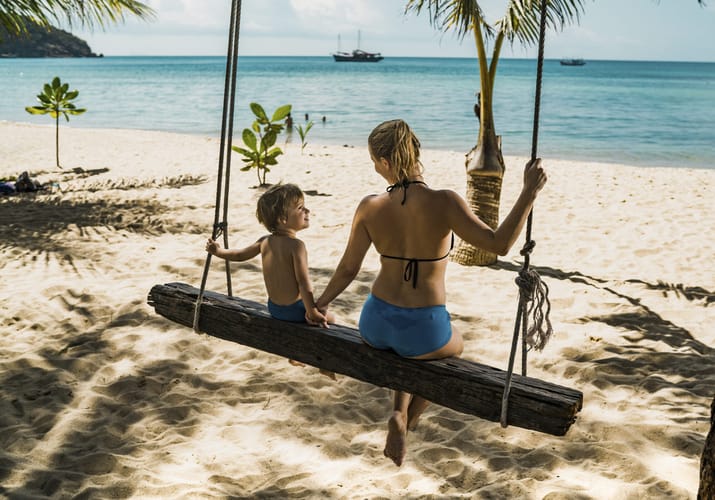Mor og søn sidder på en gynge på en strand i Thailand