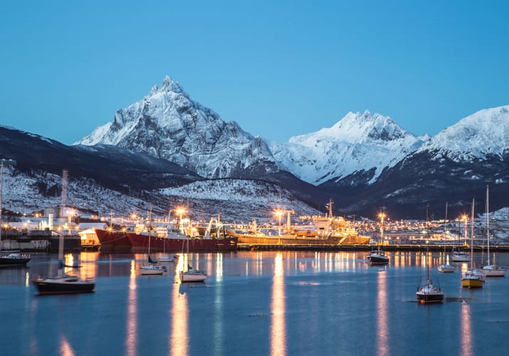 Aftenlys over Ushuaia med oplyst havn, både og snedækkede bjerge i Patagonien
