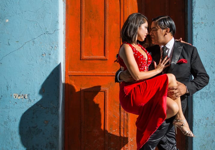 Tango-par i rød kjole danser foran farverig husfacade i Buenos Aires