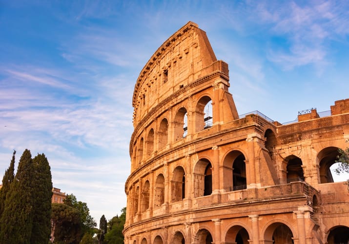 Colosseum i Rom badet i varmt aftenslys med bl&aring; himmel over