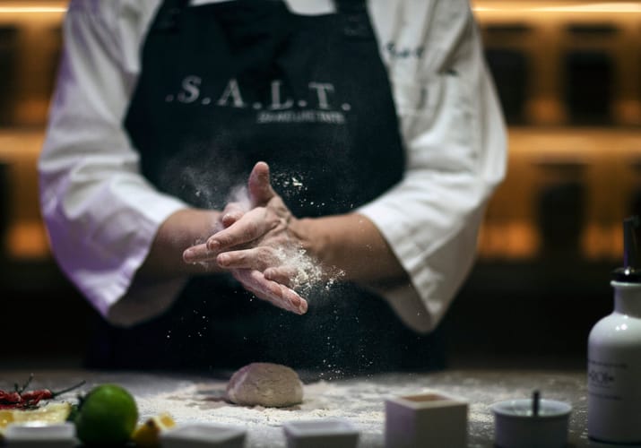 Kok i S.A.L.T.-køkkenet former dej og drysser mel under kulinarisk oplevelse ombord
