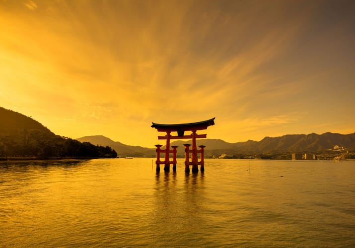 Den ber&oslash;mte r&oslash;de Torii-port ved Miyajima havn under gylden solnedgangshimmel