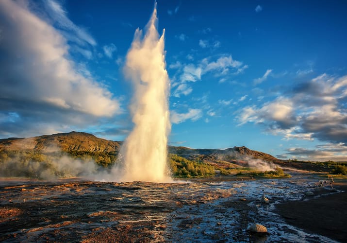 Strokkur geysir på Island der sprøjter varmt vand højt op i luften mod blå himmel med dramatiske skyer